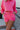 Close-up front view of model wearing the Out Of Your League Shorts which feature a hot pink material, an elastic waist band with adjustable ties, front pockets, a patchwork design, and two back pockets