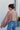 Back view of the Born Lucky that features a taupe colored material, a surplice neckline with a button closure, an oversized long sleeve with an adjustable tie detail at the wrist, and a back elastic hem line.