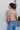 Back view of the Born Lucky that features a taupe colored material, a surplice neckline with a button closure, an oversized long sleeve with an adjustable tie detail at the wrist, and a back elastic hem line.
