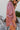 Side view of model wearing the Always On My Mind Top, which features a mauve satin material, a collared neckline, a gold button-up front, long cuffed sleeves, a high-low design, and a flowy fit. Top is tucked into shorts.