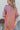 Back view of model wearing the Always On My Mind Top, which features a mauve satin material, a collared neckline, a gold button-up front, long cuffed sleeves, a high-low design, and a flowy fit. Top is tucked into shorts.
