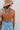 Back view of the Knot Yours Bodysuit that features a camel colored material, a round neckline, a long sleeve, a knot cut-out detail at the chest, a thong bottom, and a snap closure.