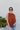 Front view of model wearing the Falling For You Top, which features a rust colored material, a rounded neck with a ruffle detail, a smocked top, a sleeveless design with thick straps, a flowy fit, and a back button closure a the neck