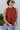 Close-up front view of model wearing the Falling For You Top, which features a rust colored material, a rounded neck with a ruffle detail, a smocked top, a sleeveless design with thick straps, a flowy fit, and a back button closure a the neck