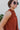 Close-up side view of model wearing the Falling For You Top, which features a rust colored material, a rounded neck with a ruffle detail, a smocked top, a sleeveless design with thick straps, a flowy fit, and a back button closure a the neck