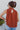 Back view of model wearing the Falling For You Top, which features a rust colored material, a rounded neck with a ruffle detail, a smocked top, a sleeveless design with thick straps, a flowy fit, and a back button closure a the neck