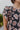 Frontal view of the Untamed Florals Top that features a black colored material, a floral print, a round neckline, a short ruffle sleeve, smock detailing at the shoulders, a back button closure, and a flowy fit.