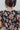 Back view of the Untamed Florals Top that features a black colored material, a floral print, a round neckline, a short ruffle sleeve, smock detailing at the shoulders, a back button closure, and a flowy fit.