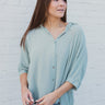 Frontal view of the Back In Session Top In Spruce that features a sage colored material, a collar neckline, a button-up front, an oversized half sleeve, a high-low design, and a flowy fit.