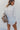 Back view of the Jump Start Top that features a white colored material, a collar neckline, a button-up front, a cuffed long sleeve, a front pocket a high-low design, and a flowy fit.
