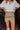 Frontal view of the New In Town Skirt that features a tan faux-leather material, a high-rise fit, a draped side, a surplice front, a drape side detail, a back zipper closure, and a mini length