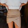 Frontal view of the New In Town Skirt that features a tan faux-leather material, a high-rise fit, a draped side, a surplice front, a drape side detail, a back zipper closure, and a mini length