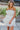 Frontal view of the Tulle Me About It Mini Dress that features a cream tulle material with a straight neckline, a sleeveless tiered design, a side zipper closure, and a mini length