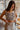 Frontal view of the Check Mate Crop Top that features a brown and white checkered print, a straight neckline, a sleeveless design with thin straps, a cropped fit, and a back zipper closure.