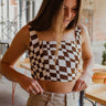 Frontal view of the Check Mate Crop Top that features a brown and white checkered print, a straight neckline, a sleeveless design with thin straps, a cropped fit, and a back zipper closure.
