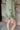 Frontal view of the On To The Next Top that features an olive green satin material, a collar neckline, a long sleeve with feather detailing at the cuff, a button-up front, and a flowy fit.