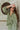 Frontal view of the On To The Next Top that features an olive green satin material, a collar neckline, a long sleeve with feather detailing at the cuff, a button-up front, and a flowy fit.