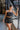 Frontal view of the One To Watch Skort that features a black faux-leather material, a thick elastic waist band with a tie detail, a tiered ruffle design, a shorts lining, and a flowy fit.