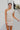 Frontal view of the Big Plans Mini Dress that features an ecru faux-leather material, an asymmetrical neckline, a sleeveless design with a one shoulder strap, a ruched side detail, and a side zipper closure.