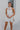 Frontal View of the Seek It Out Mini Dress that features a white colored material, a sleeveless design with a high halter neck, a mesh material at the chest, an open back, and a back zipper closure.