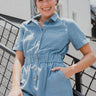 Frontal View of the Heading South Romper that features a blue colored material, a collar neckline, a short cuffed sleeve, a button-up front, two front pockets at the chest, a cinched waist, two side pockets, cuffed bottom hem, and two back pockets.