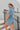 Back View of the Heading South Romper that features a blue colored material, a collar neckline, a short cuffed sleeve, a button-up front, two front pockets at the chest, a cinched waist, two side pockets, cuffed bottom hem, and two back pockets.