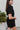Side view of the Heading South Romper that features a black colored material, a collar neckline, a short cuffed sleeve, a button-up front, two front pockets at the chest, a cinched waist, two side pockets, cuffed bottom hem, and two back pockets.