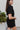 Side view of the Heading South Romper that features a black colored material, a collar neckline, a short cuffed sleeve, a button-up front, two front pockets at the chest, a cinched waist, two side pockets, cuffed bottom hem, and two back pockets.