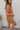 Side view of the Lady May Romper that features a brown fabric, a collar neckline, a short cuffed sleeve, a button-up front, two front pockets at the chest, a cuffed bottom hem, and two back pockets.
