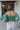 Back view of the In The Air Top that features a green colored metallic material, a V neckline, a half puffy sleeve, a ruched front, a smocked back, and a cropped fit.