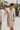 Frontal view of the Means Business Dress that features a cream colored chiffon material, a surplice lapel neckline, a long sleeve, a wrap front with a tie, and a mini length.