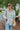 Frontal view of the Summer Soiree Top that features a white colored material, a multi-colored print, a collar neckline, a button-up front, a long cuffed sleeve, and a front pocket.