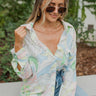 Frontal view of the Summer Soiree Top that features a white colored material, a multi-colored print, a collar neckline, a button-up front, a long cuffed sleeve, and a front pocket.