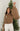 Front view of model wearing the Next Adventure Puffer Jacket in Brown that has a brown nylon material, a puffer design, a long sleeve, a zip-up front, and front pockets. Model holding a pouch.