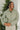 Front view of model wearing the New Adventure Puffer Jacket in Moss that has a moss green nylon material, a puffer design, a long sleeve, a zip-up front, and front pockets. Model holding a packable pouch!