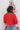 Back view of model wearing the he Holiday Spirit Mock Neck Sweater that has red fabric with open knit details, a mock neckline, dropped shoulders, long sleeves, and ribbed trim.