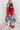 Full body front view of model wearing the he Holiday Spirit Mock Neck Sweater that has red fabric with open knit details, a mock neckline, dropped shoulders, long sleeves, and ribbed trim.