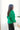 Side view of model wearing the Merry And Bright Sweater that has green knit fabric, a cropped waist, a ruched drawstring front, a v neckline, and long balloon sleeves.