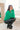 Side view of model wearing the Merry And Bright Sweater that has green knit fabric, a cropped waist, a ruched drawstring front, a v neckline, and long balloon sleeves.
