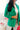 Close front view of model wearing the Business As Usual Blazer in Green that has a green material with a full lining, a lapel and a collar, shoulder pads, cuffed sleeves, and faux front pockets. Worn over white top.