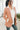 Frontal/side view of model wearing the Business As Usual Blazer in Blush that has a dusty pink material with a full lining, a lapel and a collar, shoulder pads, cuffed sleeves, and faux front pockets. Worn over white blouse.