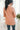 Back view of model wearing the Business As Usual Blazer in Blush that has a dusty pink material with a full lining, a lapel and a collar, shoulder pads, cuffed sleeves, and faux front pockets. Worn over white blouse.