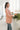 Side view of model wearing the Business As Usual Blazer in Blush that has a dusty pink material with a full lining, a lapel and a collar, shoulder pads, cuffed sleeves, and faux front pockets. Worn over white blouse.