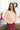 Front view of model wearing the No Plans Pullover in Pink that has light pink waffle-knit fabric, long batwing sleeves, a hood with an ivory drawstring, and a wide fit