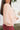 Side view of model wearing the No Plans Pullover in Pink that has light pink waffle-knit fabric, long batwing sleeves, a hood with an ivory drawstring, and a wide fit