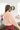 Back view of model wearing the No Plans Pullover in Pink that has light pink waffle-knit fabric, long batwing sleeves, a hood with an ivory drawstring, and a wide fit