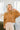 Front view of model wearing the No Plans Pullover in Brown that has light brown waffle-knit fabric, long batwing sleeves, a hood with an ivory drawstring, and a wide fit