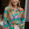 Front view of model wearing the Having A Good Day Top that has turquoise plisse fabric with a multicolor floral pattern, a ruffled hem, a cropped waist, a button-up front, a collar, and long sleeves with ruffled hems.