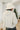 Back view of model wearing the No Plans Pullover in Beige that has beige waffle-knit fabric, long batwing sleeves, a hood with an ivory drawstring, and a wide fit