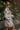 Side  view of model wearing the Look On The Bright Side Dress that has a pink, green, blue, yellow and cream flower pattern, a mini-length hem, an elastic waist with a tie, a surplice neck, and long balloon sleeves.
